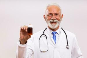 retrato do Senior médico mostrando garrafa do pílulas em cinzento fundo foto