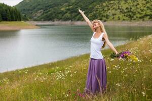 mulher com dela braço elevado goza dentro a natureza e segurando ramalhete do flores foto