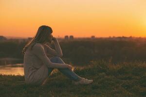 triste mulher sentado às a pôr do sol e pensamento. foto