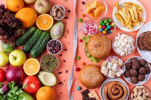 frutas e vegetais vs doces e fast food vista superior plana sobre fundo laranja foto