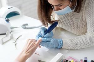 mestre de manicure usando uma máquina elétrica para remover o esmalte durante a manicure no salão foto