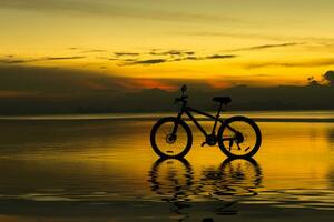 silhueta do uma bicicleta em uma lago às crepúsculo. foto