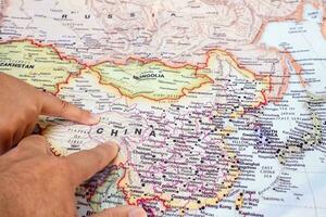 turista mão apontando às mundo mapa do China. localizado dentro Ásia em mundo mapa, China é uma país com uma ampla área e uma ampla população. topo Visão foto
