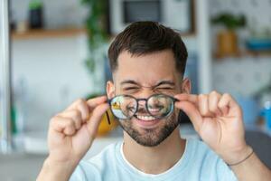 jovem homem detém óculos com dioptria lentes e parece através eles, a problema do miopia, visão correção foto