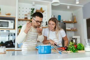 afetuoso jovem homem se beijando dele esposa enquanto ela é fazer o jantar. lindo jovem casal é falando e sorridente enquanto cozinhando saudável Comida dentro cozinha às lar. foto