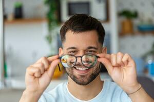 jovem homem detém óculos com dioptria lentes e parece através eles, a problema do miopia, visão correção foto