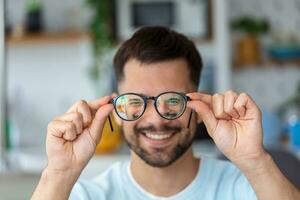 jovem homem detém óculos com dioptria lentes e parece através eles, a problema do miopia, visão correção foto