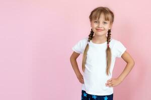 lindo pequeno Loiras menina com grandes cabelo dentro branco camiseta sorridente em uma Rosa fundo foto