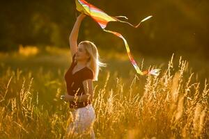 beleza menina corrida com pipa em a campo. lindo jovem mulher com vôo colorida pipa sobre Claro azul céu. livre, liberdade conceito. emoções, saudável estilo de vida foto