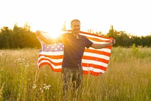 quarto do julho. patriótico homem com a nacional americano bandeira dentro a campo. jovem homem orgulhosamente acenando a americano bandeira. independência dia. foto