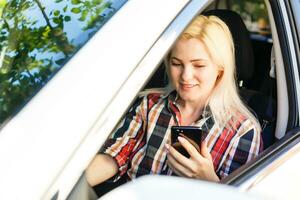 jovem mulher olhando para dela Smartphone enquanto dirigindo carro foto