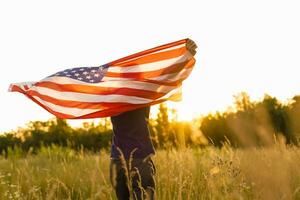 quarto do julho. patriótico homem com a nacional americano bandeira dentro a campo. jovem homem orgulhosamente acenando a americano bandeira. independência dia. foto