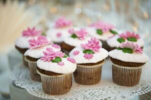 bolo para uma bufê mesa. uma grupo do pequeno bolos de copo decorado com Rosa creme flores foto