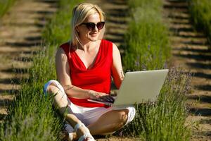 eufórico mulher procurando trabalho com uma computador portátil dentro a urbano parque dentro verão foto