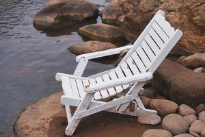 cadeira de praia de madeira branca colocada em uma rocha ao lado do rio foto