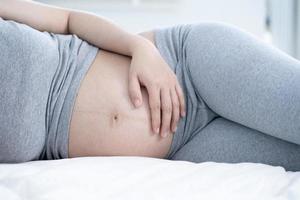 mulher grávida dormindo na cama em casa. close-up de uma mulher grávida deitada na cama e tocando sua barriga foto