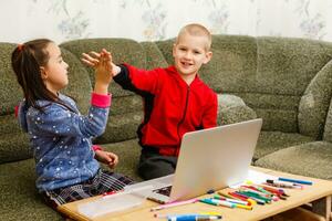 dois lindo fofa feliz sorridente crianças, uma Garoto e uma garota, usar computador portátil para distância Aprendendo ou entretenimento. foto