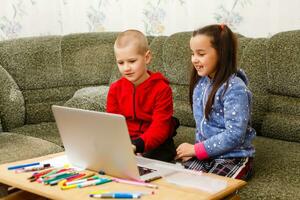 distância Aprendendo conectados Educação. escola Garoto e menina estudando às casa com computador portátil caderno e fazendo trabalho de casa. sentado às uma mesa foto