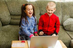 dois lindo fofa feliz sorridente crianças, uma Garoto e uma garota, usar computador portátil para distância Aprendendo ou entretenimento. foto