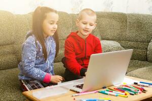 dois lindo fofa feliz sorridente crianças, uma Garoto e uma garota, usar computador portátil para distância Aprendendo ou entretenimento. foto