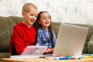 dois lindo fofa feliz sorridente crianças, uma Garoto e uma garota, usar computador portátil para distância Aprendendo ou entretenimento. foto