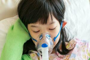 doente pequeno ásia menina inalação com nebulizador para respiratório tratamento foto