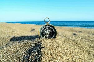 uma bússola em a de praia com a oceano dentro a fundo foto