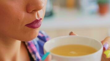 caucasiano jovem mulher tentando para beber quente verde chá. fechar acima do bonita senhora sentado dentro a cozinha dentro a manhã durante café da manhã Tempo relaxante com saboroso natural ervas chá a partir de branco xícara de chá. foto