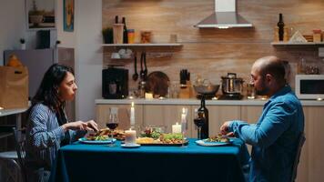 amantes jantar junto, comendo e bebendo vinho durante festivo jantar dentro a cozinha. feliz casal conversando, sentado às mesa desfrutando refeição às casa tendo romântico Tempo juntos surpresa vela luzes foto