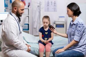 médico falando sobre diagnóstico e tratamento com mãe do criança dentro médico escritório. praticante pediatra especialista dentro remédio fornecendo profissional healtcare Serviços foto