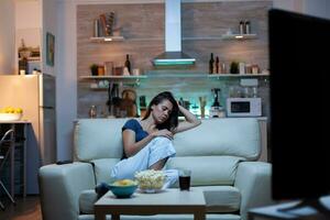 cansado dona de casa queda adormecido dentro frente do televisão sentado em acolhedor sofá dentro vivo sala. Exausta solitário sonolento entediado mulher dentro pijamas dormindo em sofá enquanto assistindo televisão casa sozinho atrasado às noite foto