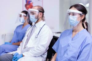 retrato do médico funcionários dentro uniforme e protetora mascarar olhando às Câmera. equipe do profissional remédio trabalhadores dentro segurança mascarar posando às Câmera juntos sentado dentro Novo normal hospital foto