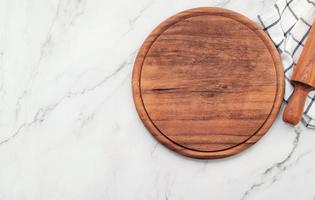 bandeja de pizza de madeira vazia com guardanapo e rolo na mesa da cozinha de pedra de mármore. placa de pizza e toalha de mesa em fundo de mármore branco. foto