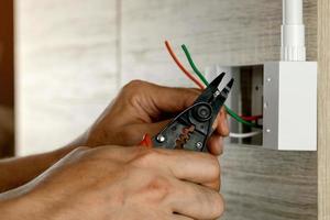 eletricista está removendo fios elétricos em uma caixa de plástico em uma parede de madeira para instalar a tomada elétrica. foto