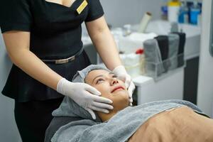 fechar-se cosmetologistas preparar clientes face antes fazer facial massagem com orgânico face esfregar e suave facial branco mascarar creme foto