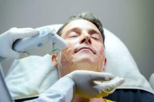homem bonito closeup tendo terapia de luz colorida para estimular a pele facial pelo bem-estar cosmetologista profissional. foto