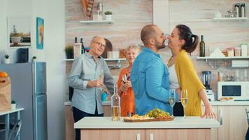 alegre maduro casal abraçando paquera dentro cozinha em frente Senior pais, bebendo uma branco vinho. jovem família romântico, engraçado, tendo ternura e afeição momento dentro moderno, luxo jantar quarto foto