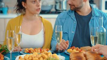 estendido feliz família brindar durante a jantar sentado às a mesa dentro a cozinha. óculos do branco vinho visto durante uma acolhedor festa do uma celebração. foto