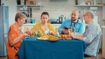 homem usando telefone durante jantar mostrando alguns As fotos para dela mãe. multi geração, quatro pessoas, dois feliz casais falando e comendo durante uma gourmet refeição, desfrutando Tempo às lar.