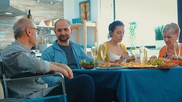 paralisado avô a comemorar dele aniversário com dele família sentado às a cozinha mesa. feliz casais sorridente, bebendo vinho e comendo durante uma gourmet refeição, desfrutando relaxante Tempo foto