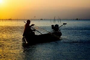 silhueta pescador e pôr do sol céu em a lago. foto