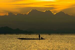 silhueta pescador e pôr do sol céu em a lago. foto