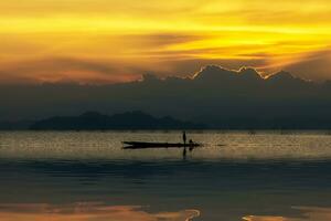 silhueta pescador e pôr do sol céu em a lago. foto