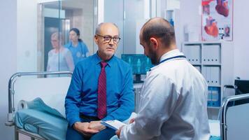 Senior homem consultando com médico sentado em hospital cama. eu vou envelhecido paciente procurando médico adendo para doença prevenção a partir de geral praticante dentro moderno privado clínica, médico diagnóstico foto