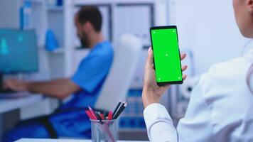 médico médico segurando Smartphone com brincar dentro hospital gabinete enquanto masculino enfermeira é trabalhando em computador. cuidados de saúde especialista dentro hospital gabinete usando Smartphone com brincar. foto