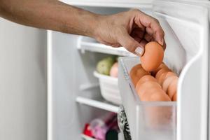 mãos humanas colocam ovos de galinha no compartimento de postura da geladeira. foto