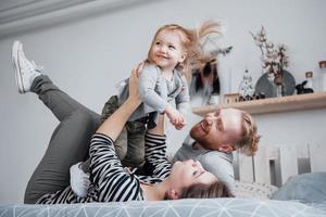 família feliz mãe, pai e filha rindo na cama foto