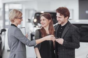 comprando seu primeiro carro juntos. visão de alto ângulo de um jovem vendedor de carros na concessionária contando aos clientes sobre as características do carro foto