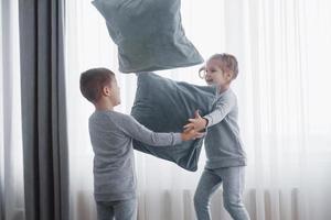 menino e menina encenaram uma luta de travesseiros na cama no quarto. crianças travessas batem umas nas outras nos travesseiros. eles gostam desse tipo de jogo foto