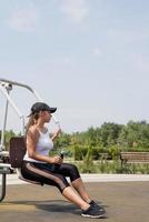 mulher feliz malhando na quadra de esportes em um dia ensolarado de verão, bebendo água da garrafa, descansando foto